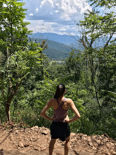 Craven Gap Hiking Trail with brunette white woman in hiking clothes looking out at the Blue Ridge Mountains