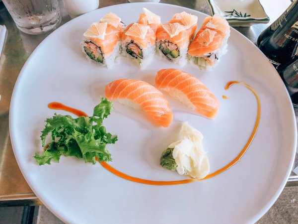 Zen Sushi Asheville NC with large white plate, two salmon sashimi, and a sushi roll topped with raw salmon and lemon wedges.