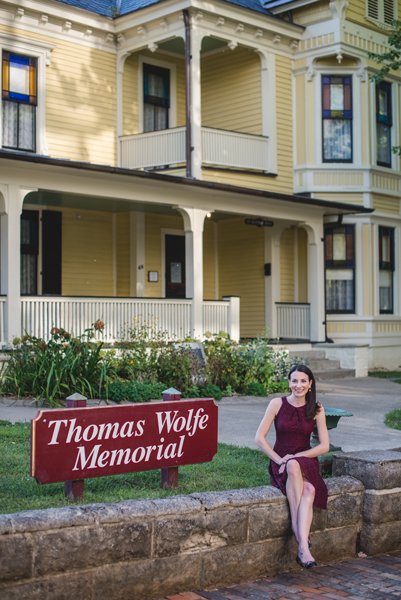 Thomas Wolfe Memorial Asheville NC yellow home with stained glass windows and brunette woman sitting out front in a maroon dress